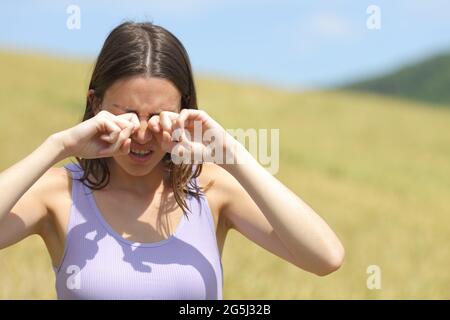 Vue de face d'une femme allergique qui se gratte les yeux dans un champ de blé Banque D'Images