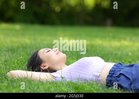 Femme de race mixte se détendant sur l'herbe dans un parc vert Banque D'Images