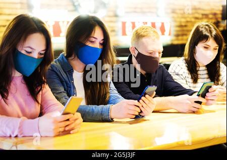 Un groupe d'amis est assis dans un bar et regarde le téléphone - le concept d'une nouvelle normalité pendant la pandémie de covid 19 jeunes dans un café Banque D'Images