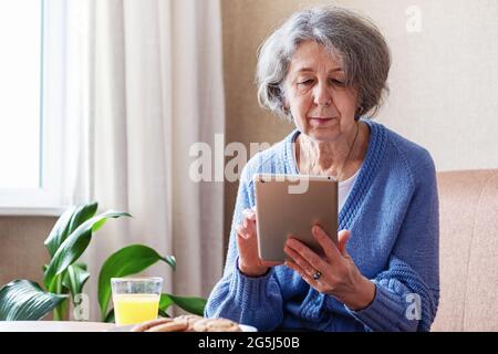 Une femme âgée utilise une tablette pour visualiser du contenu sur les réseaux sociaux - personnes âgées et technologies modernes - UNE grand-mère dans une pièce avec un gadget Banque D'Images