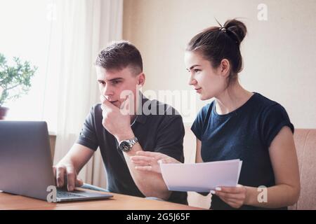 Jeune couple gère la budgétisation des finances et le suivi des dépenses - mari et femme regardent par leurs comptes bancaires et faire des paiements en ligne usi Banque D'Images