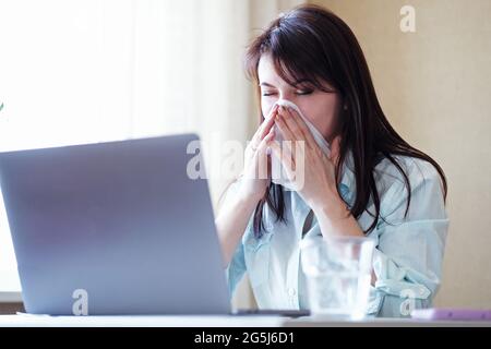 Une jeune femme malade souffle le nez à un ordinateur portable dans le bureau - UNE fille est malade et essuie son nez avec une serviette - un employé malsain souffre d'un A. Banque D'Images