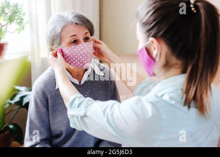 Une fille adulte met un masque sur son visage pour une mère âgée au milieu de l'épidémie du coronavirus - la petite-fille prend soin de sa grand-mère pour protéger Banque D'Images