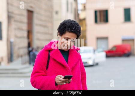 Italie, Toscane, Pistoia, femme en manteau rose utilisant le smartphone dans la rue Banque D'Images