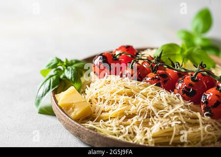 Spaghetti, pâtes avec une branche de tomates cerises grillées au basilic et au parmesan sur fond de béton léger. Mise au point sélective, espace de copie Banque D'Images