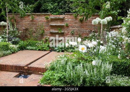 Patio en briques à chevrons, mur en briques récupéré, élément d'eau de rill, cubes de boîte et plantation blanche, aquilegias, alliums, géraniums et roses Banque D'Images