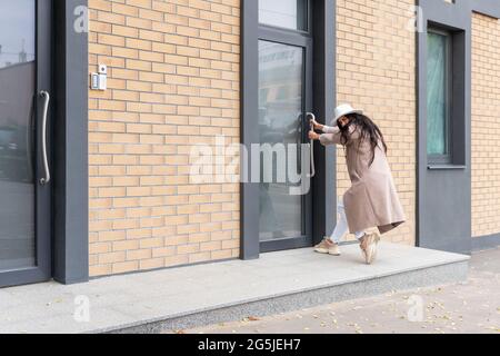 femme dans un manteau et chapeau essaie d'ouvrir une porte fermée, tire la porte par la poignée Banque D'Images