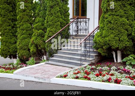 un escalier en granit avec des rampes en fer forgé, des marches d'entrée, sortie vers l'arrière-cour avec un lit fleuri et des thuja à feuilles persistantes, personne Banque D'Images