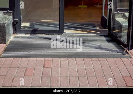 entrée au magasin depuis un trottoir piétonnier depuis une pliche sur un tapis de sol à travers une porte en verre, la façade de l'extérieur d'un bâtiment en gros plan Banque D'Images