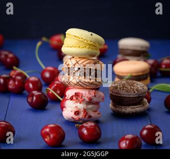 pile de macarons multicolores et de cerises rouges mûres sur fond de bois bleu Banque D'Images