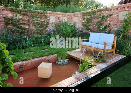 Canapé extérieur dans un petit jardin de cuisine clos, arbres fruitiers en espaliers, étang en brique formelle, boulettes d'abeilles dans le mur Banque D'Images