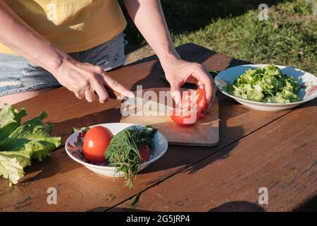 Une fille coupe de la tomate sur un panneau de bois. Cuisiner dans la nature. Banque D'Images