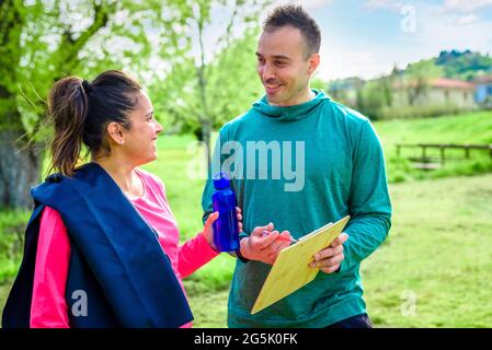 couple d'entraîneur personnel et une jeune étudiante femme enceinte discutant de l'horaire d'entraînement ensemble souriant en plein air. forme physique et mode de vie sain Banque D'Images