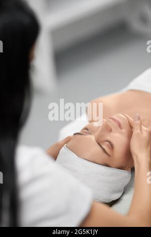 Vue de l'épaule d'un jeune esthéticienne faisant une procédure spéciale pour améliorer la peau dans un salon de beauté professionnel. Concept de jeune femme sur le massage pour le cou et le corps. Banque D'Images
