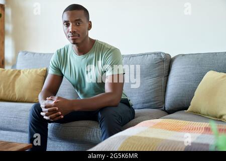 Jeune Africain assis sur son canapé de salon à la maison Banque D'Images