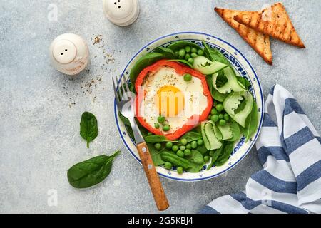 Poivrons rouges farcis avec des œufs, des feuilles d'épinards, des pois verts et des microverts sur une assiette de petit déjeuner sur fond de table gris clair. Vue de dessus. Banque D'Images