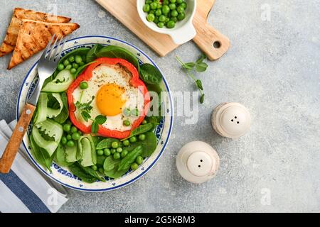 Poivrons rouges farcis avec des œufs, des feuilles d'épinards, des pois verts et des microverts sur une assiette de petit déjeuner sur fond de table gris clair. Vue de dessus. Banque D'Images