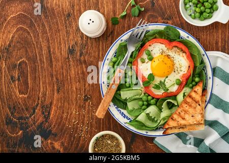 Poivrons rouges farcis avec des œufs, des feuilles d'épinards, des pois verts et des microverts sur une assiette de petit déjeuner sur fond de table en bois. Vue de dessus. Banque D'Images