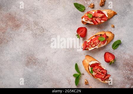 Sandwichs ouverts avec fraises, fromage doux à la menthe et aux noix dans une assiette en céramique sur fond de pierre gris clair. Nourriture estivale et saine, légumes Banque D'Images