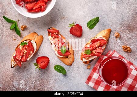 Sandwichs ouverts avec fraises, fromage doux à la menthe et aux noix dans une assiette en céramique sur fond de pierre gris clair. Nourriture estivale et saine, légumes Banque D'Images