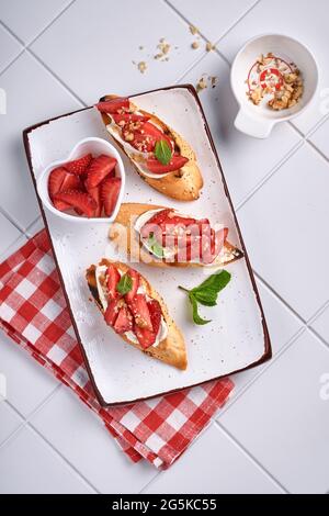 Sandwichs ouverts avec fraises, fromage doux à la menthe et aux noix dans une assiette en céramique sur fond de pierre gris clair. Nourriture estivale et saine, légumes Banque D'Images