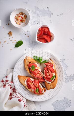 Sandwichs ouverts avec fraises, fromage doux à la menthe et aux noix dans une assiette en céramique sur fond de pierre gris clair. Nourriture estivale et saine, légumes Banque D'Images