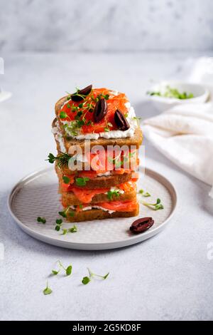 Sandwichs avec olives de saumon rose fumé, kalamata, micro-verts et fromage à la crème sur plaque en céramique grise et fond de béton tendance. SC traditionnel Banque D'Images