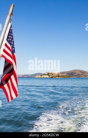 Les étoiles et les rayures des États-Unis d'Amérique volent depuis la poupe d'un bateau qui passe devant l'île de la prison d'Alcatraz. San Francisco, Californie, États-Unis Banque D'Images