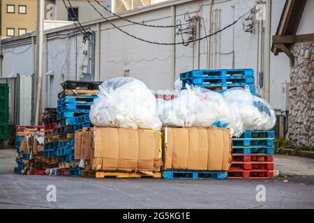 Recyclables dans une allée entre les magasins dans le centre commercial avec des paquets de boîtes décomposées des piles de palettes en bois et d'énormes sacs en plastique de plastique a Banque D'Images