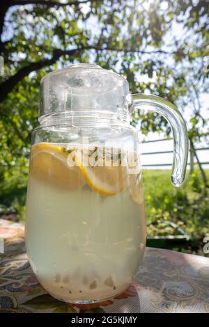 Limonade faite maison à base de citrons dans une grande carafe en verre sur la table du jardin. Une carafe au citron et à la menthe se tient dans la rue contre le backdro Banque D'Images