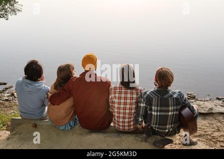 Vue arrière des amis assis à l'extérieur et appréciant le magnifique paysage du lac Banque D'Images