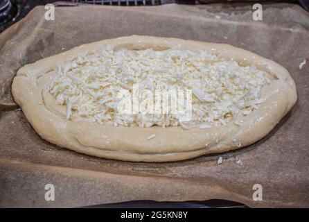 Khachapuri géorgien non cuit - UN bol à pain rempli de fromage reposant sur du papier ciré prêt pour le four - mise au point sélective. Banque D'Images