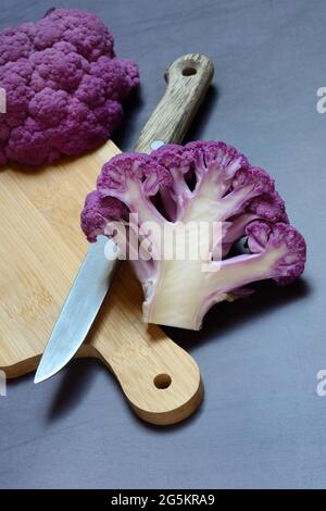 Chou-fleur violet coupé en deux sur une planche en bois avec un couteau de cuisine Banque D'Images