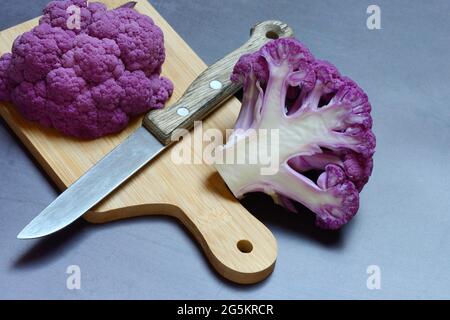 Chou-fleur violet coupé en deux sur une planche en bois avec un couteau de cuisine Banque D'Images