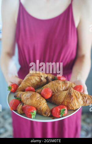 Fille tient une assiette avec des croissants et des fraises dans ses mains. Banque D'Images