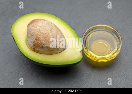 Huile d'avocat. Un avocat avec un os repose sur un plateau en pierre. L'huile d'avocat est versée dans une assiette. Bannière pour l'impression, la conception d'étiquettes, les aliments sains Banque D'Images