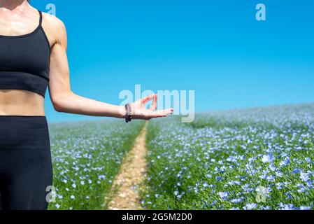 gros plan d'une femme pratiquant le yoga et la méditation dans un champ de fleurs sauvages et de ciel bleu. Banque D'Images