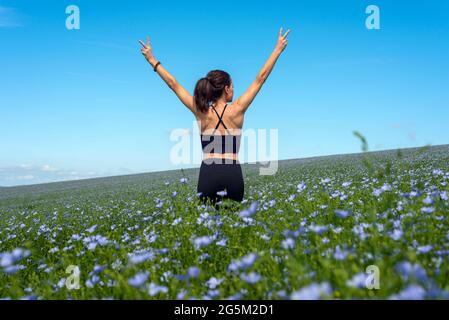 jeune femme sportive debout dans le domaine des fleurs sauvages avec les bras étirés Banque D'Images