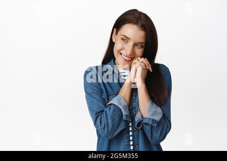 La tendresse et le concept des femmes. Mignonne et stupide fille pensant à une chose romantique, rougissant et regardant de côté, se pencher sur les mains, l'imagerie smth se sentir timide Banque D'Images