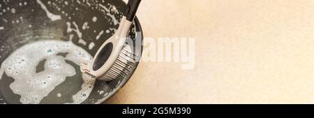 Une femme lave une poêle, une main lave une poêle dans un évier de cuisine, une brosse en silicone pour laver la vaisselle dans la main d'une femme. Placer pour le texte Banque D'Images