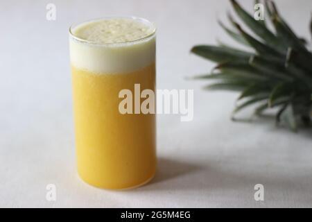 Jus d'ananas frais pour battre la chaleur estivale. Jus fait maison servi dans un long verre décoré d'un coin d'ananas. Prise de vue sur fond blanc Banque D'Images