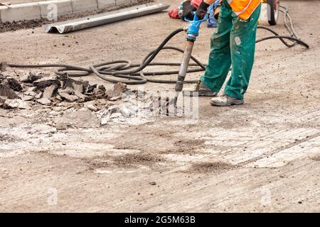Un ouvrier de la route en combinaison verte décolle l'asphalte vieux avec un marteau pneumatique sur la route un jour d'été. Copier l'espace. Banque D'Images