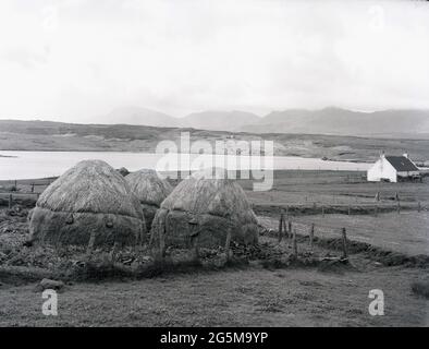 1956, historique, île de Lewis, Highlands écossais, Écosse, filet couvert de balles de foin et un chalet de ferme de crofter sur le paysage stérile. Banque D'Images