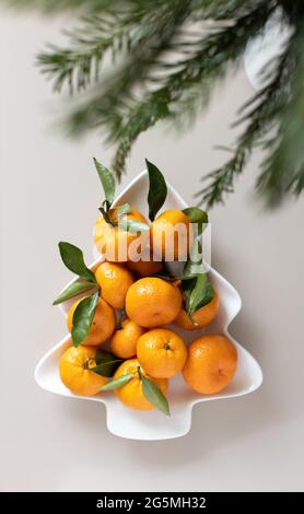 Petites mandarines mûres avec feuilles, sur plaque en forme d'arbre de Noël sur fond beige. Concept de nourriture de vitamine d'hiver. Concours festif Moody STILL Life Banque D'Images