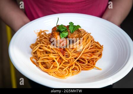 Gros plan des mains de femme tenant la sauce tomate rouge pâtes italiennes nouilles et coriandre sur la plaque blanche comme plat italien macro gros plan avec texture sur la viande Banque D'Images