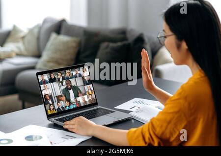 Réunion virtuelle, remue-méninges de collègues, conversation en ligne. Une jeune femme japonaise ou chinoise salue ses interlocuteurs, s'entretient par vidéoconférence avec un groupe d'affaires multiracial, discutant du projet Banque D'Images