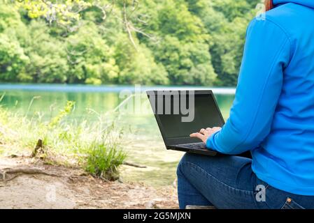 Jeune femme, femme indépendante travaillant avec un ordinateur portable avec une belle vue sur la forêt et le lac. Banque D'Images