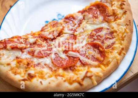 Croûte mince fraîche demi-pizza sur l'assiette avec fromage mozzarella fondu, tranches de viande de pepperoni macro-gros plan de la nourriture grasse Banque D'Images