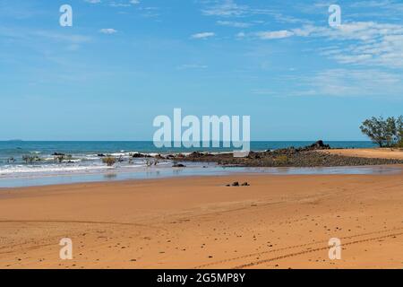 Vagues vers des rochers exposés sur une plage de sable sous un ciel bleu tandis que la marée recule Banque D'Images