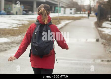 Une fille avec un sac à dos va à l'étude. Une fille dans une veste rouge descend la rue. Une femme va dans le bus. Banque D'Images